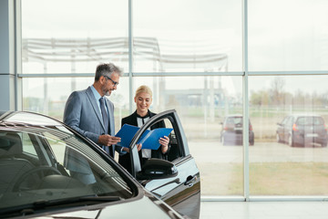 Fototapeta na wymiar senior sales agent showing car brochure to customer in car dealers showroom