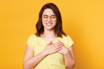 Image of charming woman keeps hands together on chest, expresses gratitude, keeps eyes closed,...