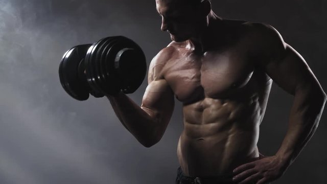 Powerful bodybuilder doing the exercises with dumbbells. Strength and motivation concept