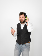 cool man with black beard and white shirt is posing with headphones and smartphone in front of white background