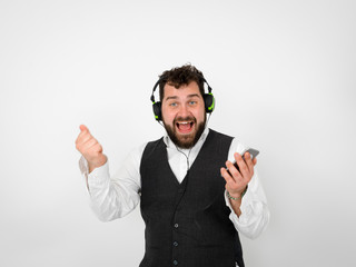cool man with black beard and white shirt is posing with headphones and smartphone in front of white background