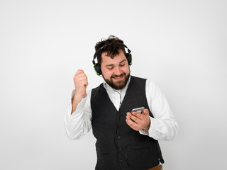cool man with black beard and white shirt is posing with headphones and smartphone in front of white background