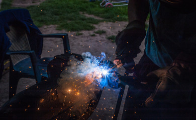 Worker with protective gloves welding metal part in workshop