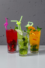 Three glasses with lemonade on a gray background. Mojito, cherry and orange.