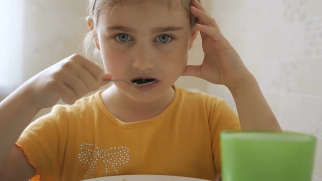 Little girl having Breakfast at home. Pretty American girl eating cereal with appetite. Child having breakfast in the kitchen. Closeup.