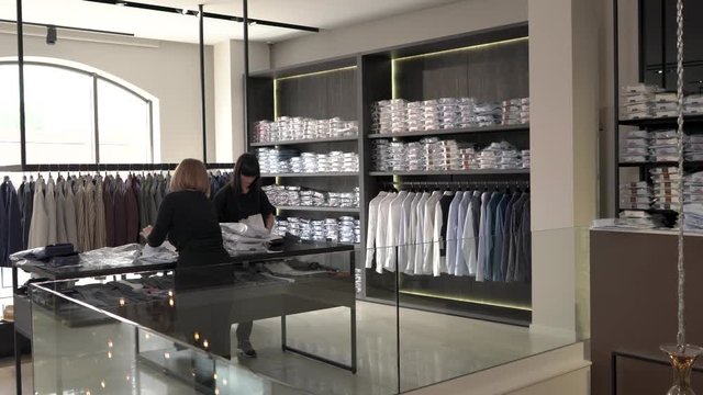 A demonstration video of shop assistants putting new collection of white male shits on the shelves. Fashion boutique routine work