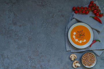 Pumpkin soup in a bowl with autumn vegetables and pumpkin seeds. Vegan soup. Vegetables cream soup and ingredients. Top view. Concept of healthy eating or vegetarian food. Top view with copy space.