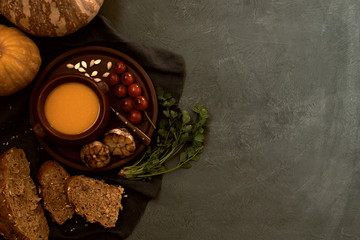 Traditional fall dishes, hot and spicy pumpkin soup with pumpkin seeds and cream on gray stone table. Autumn dinner. Organic vegetables and healthy food concept. Top view with copy space. Toned image