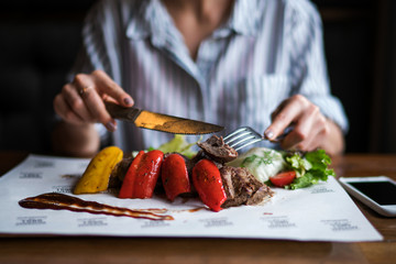 Spicy grilled lamb leg with vegetables and herbs on a roasting cast iron. Barbecue lamb with vegetables. Healthy food. Eating and leisure concept. Woman having dinner at table with food. Toned image.