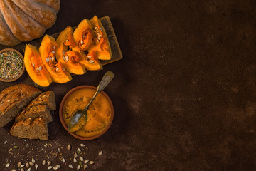 Seasonal autumn food. Spicy pumpkin ans carrot soup with cream and seasoning in rustic bowl on dark gray background. Hot, fresh vegetable soup. View from above with copy space. Toned image.