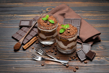 two portions Classic tiramisu dessert in a glass and chocolate bar on wooden background