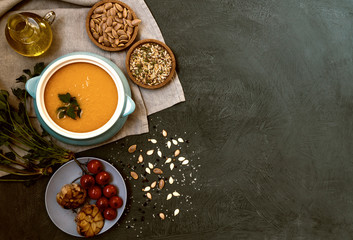 Traditional fall dishes, hot and spicy pumpkin soup with pumpkin seeds and cream on gray stone table. Autumn dinner. Organic vegetables and healthy food concept. Top view with copy space. Toned image