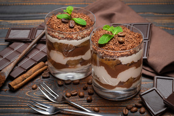 two portions Classic tiramisu dessert in a glass and chocolate bar on wooden background