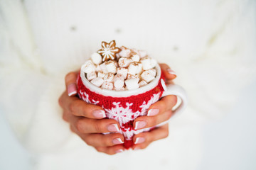 Woman holding winter cup close up on blurred lights background. Cozy mug with hot cocoa, tea or...