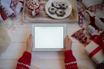 Christmas online shopping, top view. Female buys presents to prepare to christmas eve at tablet, copy space on screen. Soft winter background, knitted blanket and cake on an old vintage wooden tray.