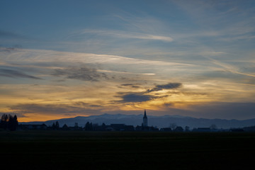 colorful sunset with different types of clouds and a hill and valley silhouette with a church tower in the austrian alps in styri