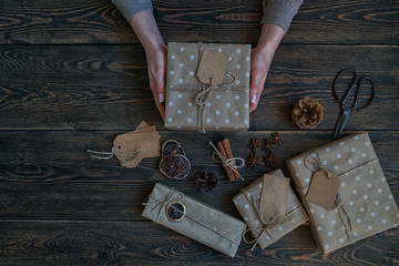 Merry Christmas and happy holidays. Woman prepare handmade gifts. Presents, decoration, fir cones, anis stars on rustic wooden background. Christmas family traditions. Selective focus. Toned image.