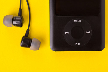Music player and headphones on a yellow background. Black headphones and player close-up. - obrazy, fototapety, plakaty