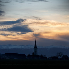 colorful sunset with different types of clouds and a hill and valley silhouette with a church tower in the austrian alps