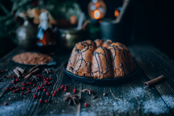 Holiday cake on wooden table with berry, spice and chocolate at rustic home kitchen. Christmas baking background. Ingredients for cooking on dark wooden background. Homemade festive food. Toned image