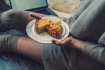 Woman eating cake at Christmas eve. Girl holding plate of christmas cake relaxing at home, drinking cacao, using laptop. Winter and Christmas holidays concept. Top view. Soft, comfy lifestyle.
