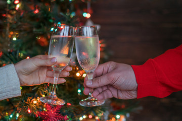 Christmas illuminations and champagne glasses. Hands of people with glasses of champagne, celebrating and toasting in honor of the Christmas and Happy New Year. Couple cheering with champagne flutes.