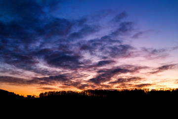 colorful sunset with glowing clouds and a tree a hill and valley silhouette in the austrian alps