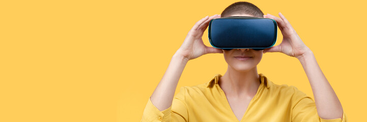 Young woman in her 30s using virtual reality goggles. Woman wearing VR headset isolated over yellow...