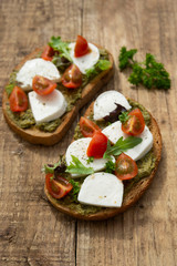 Mozzarella cheese, cherry tomatoes and pesto bruschetta, toast on wooden background. Healthy breakfast ,snack. Pesto pasta.
