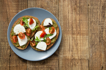 Toast sandwich mozzarella cheese, cherry tomatoes and pesto bruschetta, toast on wooden background. Healthy breakfast, snack. Copy space.
