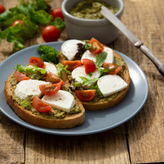 Healthy snack - mozzarella cheese, cherry tomatoes and pesto bruschetta, toast on wooden background. Healthy breakfast ,snack. Pesto pasta.