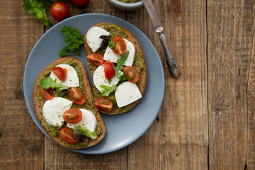 Toast sandwich mozzarella cheese, cherry tomatoes and pesto bruschetta, toast on wooden background. Healthy breakfast, snack. Copy space.