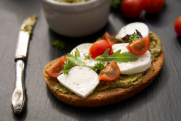 Mozzarella cheese, cherry tomatoes and pesto bruschetta, toast on black background. Healthy breakfast ,snack. Pesto pasta.