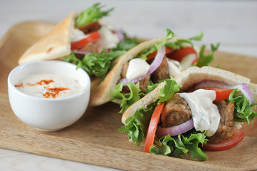 Falafel pita bread with tomatoes, lettuce and sauce. Next to the  pita bread cup with sauce. Light wooden background. Close-up. Macro shooting.
