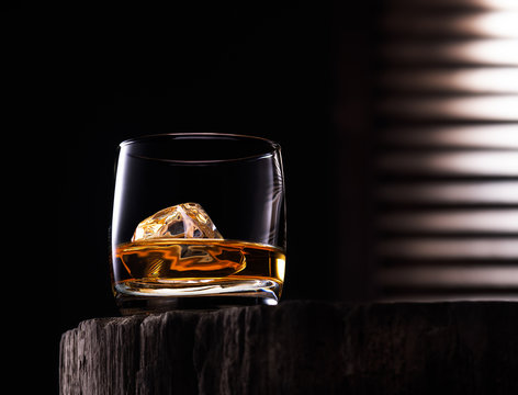 Glass of whiskey with ice cube on the wooden table with wooden background