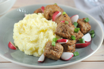 Mashed potatoes with meatballs occupy the entire space of the frame. Meatballs supplemented with radish and green onions. Macro shooting.