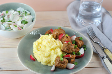 Mashed potatoes with meatballs, radishes and green onions. In a bowl, a vegetable salad with sour cream. Traditional Scandinavian lunch. Light background.