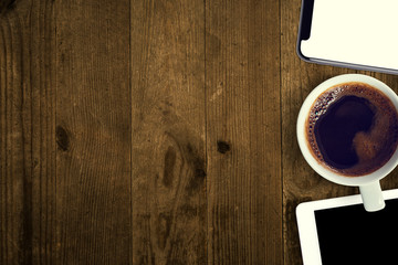 Old desk at home and on it a modern device for communication in business. Lies a flat coffee mug, tablet and smartphone on a wooden old countertop. Copy space and banner.