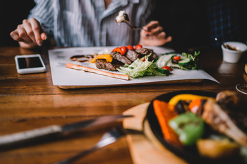 Spicy grilled lamb leg with vegetables and herbs on a roasting cast iron. Barbecue lamb with vegetables. Healthy food. Eating and leisure concept. Woman having dinner at table with food. Toned image.