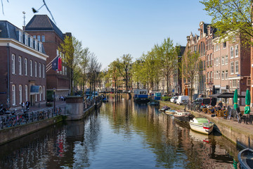 Outdoor sunny view of typical Holland brick architectures, boats and street along beautiful shady canal at red light district in spring season in the morning.