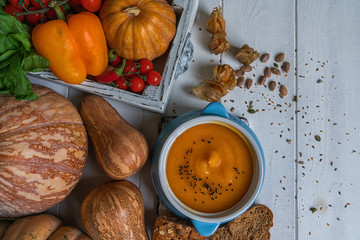 Pumpkin soup in a bowl with autumn vegetables and pumpkin seeds. Vegan soup. Vegetables cream soup and ingredients. Concept of healthy eating or vegetarian food. Top view with copy space. Toned image.