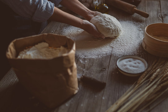 Female hands making dough for pizza. Baker kneading fresh raw dough on kitchen table. Concept of nature, Italy, food, diet and bio. Low key shot, close up on hands, some ingredients around on table.