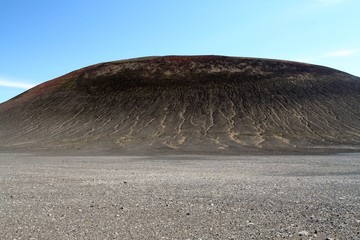 View over barren plain with nothing than small stones on bleak black hill with furrows contrasting...