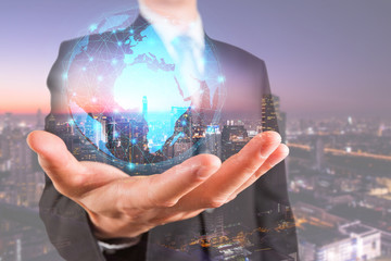 Double exposure of businessman holding the glowing polygonal hologram digital globe and cityscape in the night or twilight as business, innovation, intelligent and idea concept