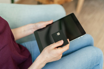 Adult woman sitting in cafe and making online shopping using tablet and card