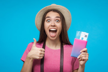 Young excited female student tourist showing thumbs up gesture, isolated on blue background. Travel...