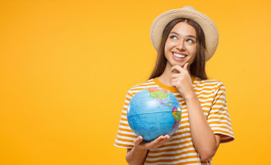 Young female dreaming about future trip, holding globe with one hand, isolated on yellow...