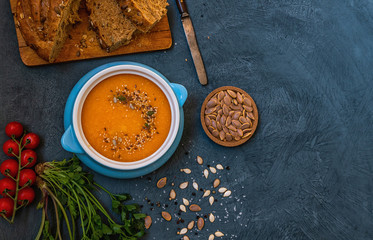 Pumpkin soup in a bowl with autumn vegetables and pumpkin seeds. Vegan soup. Vegetables cream soup and ingredients. Concept of healthy eating or vegetarian food. Top view with copy space. Toned image.