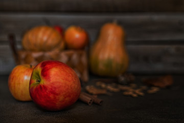 Ripe red apples with pumpkins in the basket in the background. Autumn background from yellow flowers, fruit and vegetables. Fall season, eco food and harvest concept. Selective focus. Toned image.