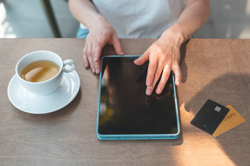 Adult woman sitting in cafe and using tablet for online shopping